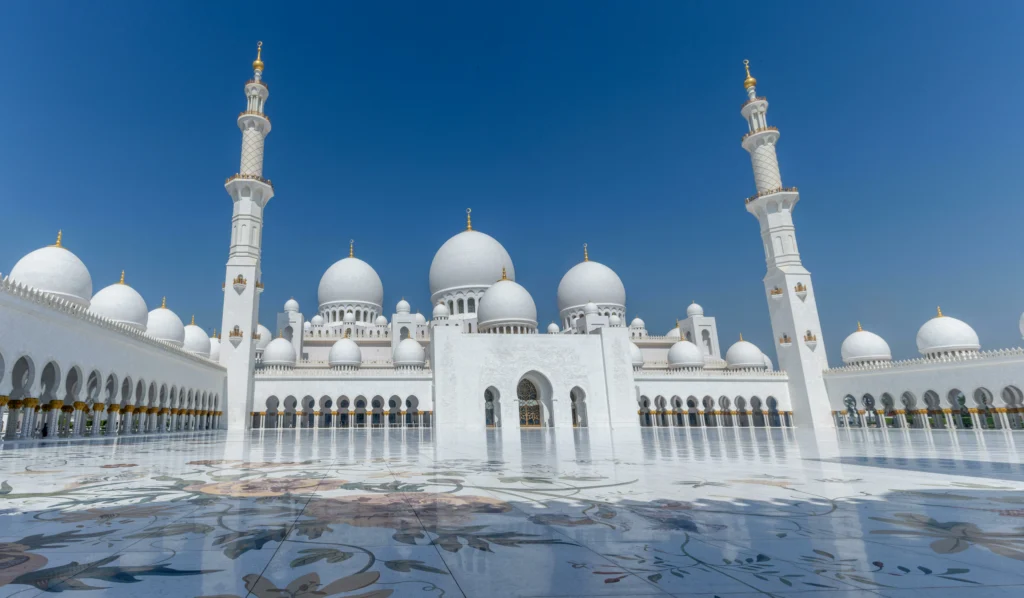 Group of tourists exploring the majestic Sheikh Zayed Grand Mosque, admiring its stunning white marble architecture, grand domes, and intricate Islamic design during a guided tour.